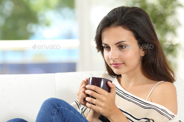 Woman thinking with a cup of coffee at home