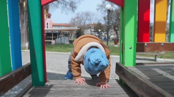 A Boy on a Playground in an Autumn Park Climbs a Hill in Cloudy Weather alt