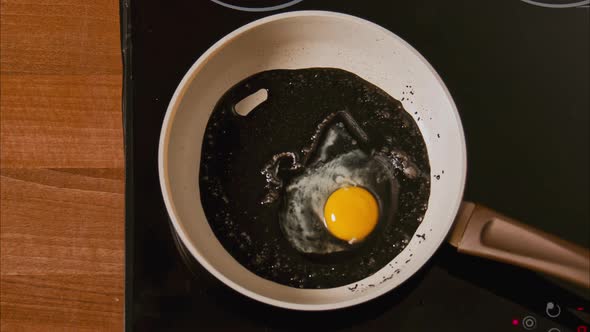 Male Hands Break an Egg Into a Frying Pan in Black Oil