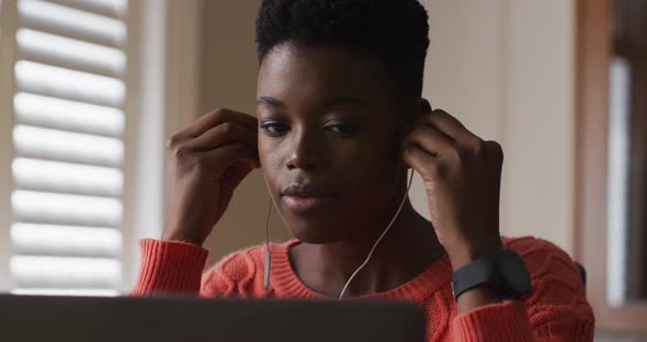African american woman wearing earphones using laptop while working from home alt