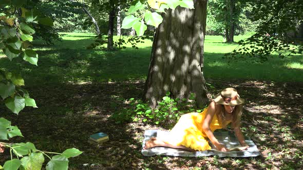 Woman Sitting on Plaid Reading a Book in Park under Tree Shadow