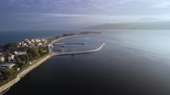 Aerial View on the Long Narrow Peninsula with Small Village and Docks with Moored Ships alt