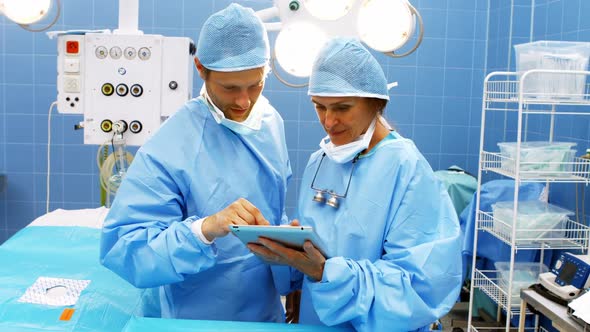 Male and female surgeons using digital tablet in operation room alt