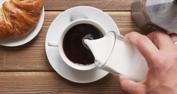 Person Pouring Milk Into Black Morning Coffee. alt