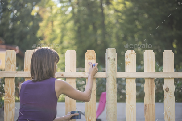 Woman varnishing a wooden picket fence - Stock Photo - Images