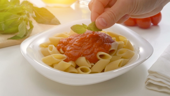 Basil Leaf Being Put On Freshly Cooked Homemade Pasta With Tomato Souce.