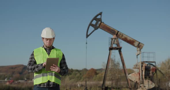 Engineer Near an Oil Pump Holding Digital Tablet and Looking at Camera alt