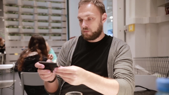Modern Technology In a Public Place. Handsome Young Man With a Beard Using His Smartphone alt