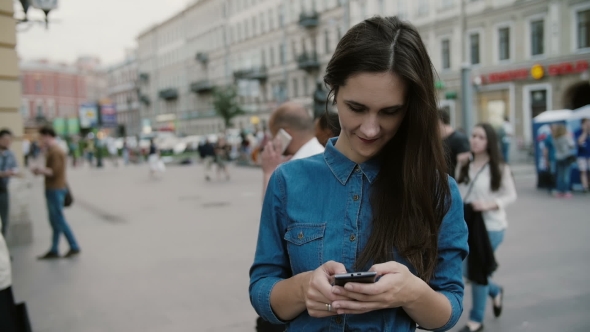 Modern Technology. Beautiful Brunette Young Woman In a Denim Dress Using Her Smartphone alt