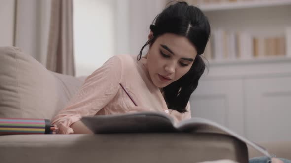 Young Female colouring book with pencil on sofa in living room