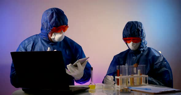 People in Protective Clothing with Hoods, Respirators, Orange Glasses and White Gloves Sit at a alt