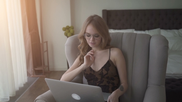 Cute Woman Working On Her Laptop While Sitting In An Armchair At Home