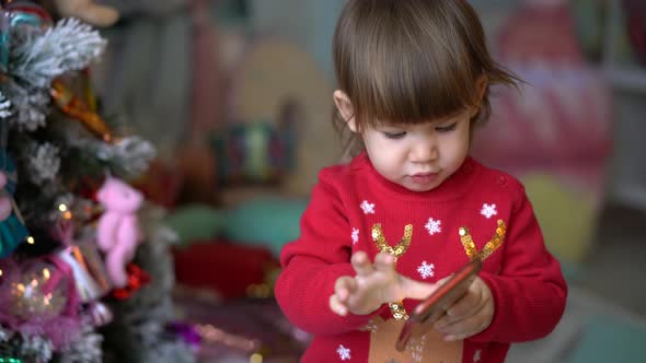 Happy Girl in a Red Sweater Plays on a Mobile Phone Against the Background alt