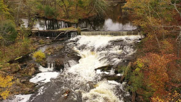 An drone view over a waterfall surrounded by colorful fall foliage in upstate NY. The camera, facing alt