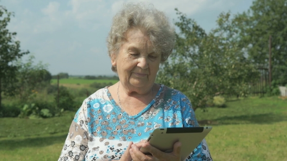 Elderly Woman Walking With Digital Tablet Outdoors