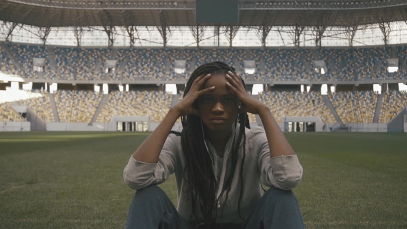 Nervous Sporty African-american Woman Sitting Alone In The Middle Og Sports Stadium And Looking To