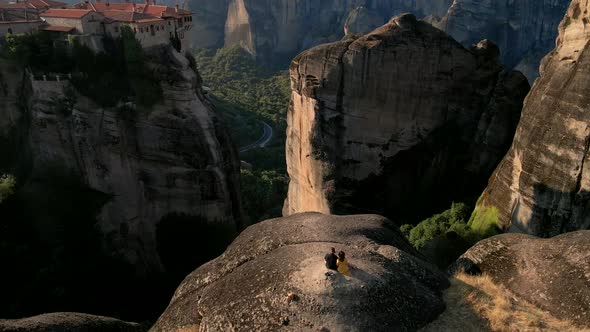 Couple Travelers Sitting on the Rocks Looking at Meteora Templates in Greece alt
