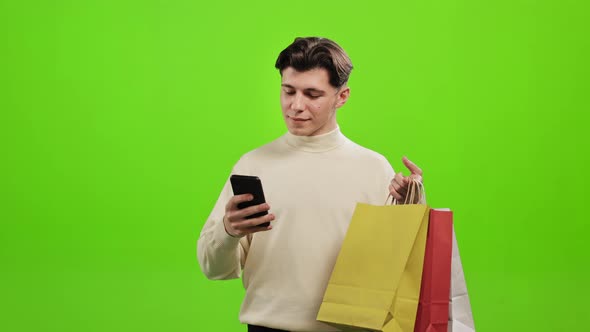 A Man is Texting on a Smartphone and Holding Shopping Bags in His Hands alt