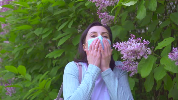 Portrait of Young Allergic Woman in Medical Mask Sneezes and Looks at Camera alt