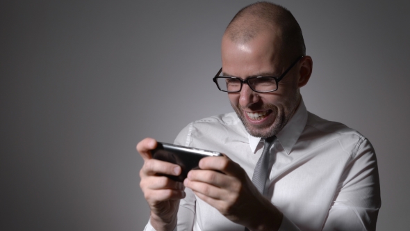 Very Expressive And Emotional Manager In White Shirt And Tie Playing Games On His Smartphone. alt