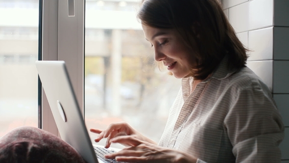 Girl Typing On a Laptop Sitting On Window