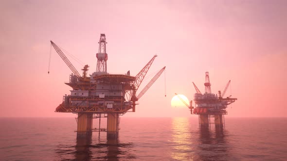 Two offshore platforms in the open sea with a pink evening sky and setting sun. alt