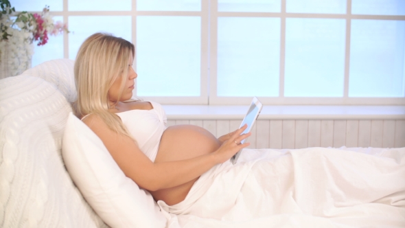 Pregnant Woman Relaxing On Bed Using Tablet