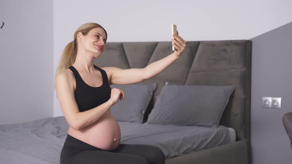 Side View of a Beautiful Pregnant Woman in Sportswear a Woman Talking on a Video Link with Her