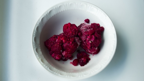 Frozen Raspberries Melting In a Plate On a White Background. alt