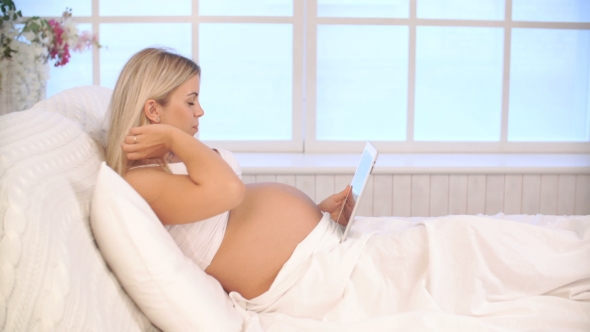 Pregnant Woman Relaxing On Bed Using Tablet