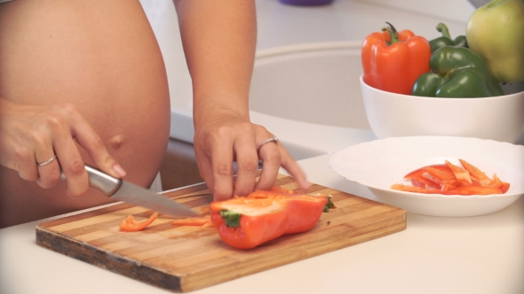 Pregnant Woman Cuts Pepper In The Kitchen. Vegetables For Salad