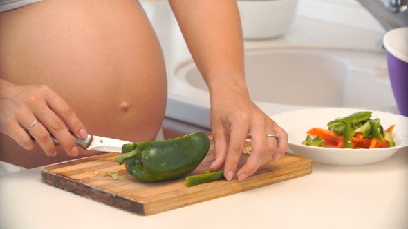 Pregnant Woman Cuts Pepper in the Kitchen. Vegetables for Salad