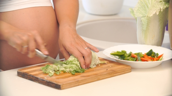 Pregnant Woman Cuts Cabbage On a Wooden Board In The Kitchen.