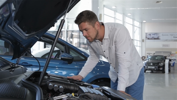 Man Looks at the Engine Compartment of the Car at the Dealership alt