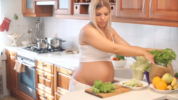 Pregnant Woman Cuts the Lettuce on Wooden Board In The Kitchen