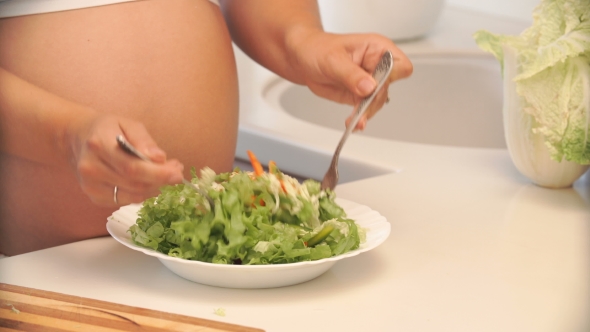 Pregnant Woman Mixing Salad In a Bowl In The Kitchen.