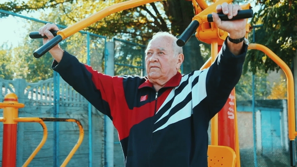 Elderly Man Exercising With Fitness Equipment In Public Outdoor Gym.