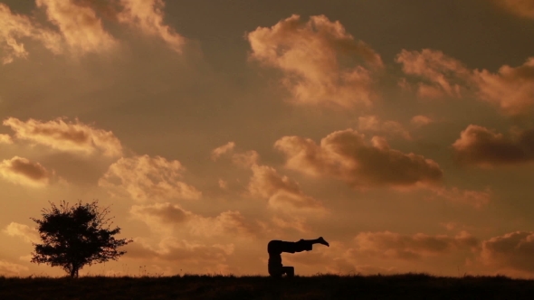 Man Doing Yoga Asanas On a Background Of Clouds And Near The Small Tree.