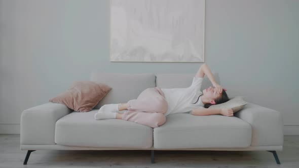 Young tired Caucasian woman with headache and migraine lying on sofa living room