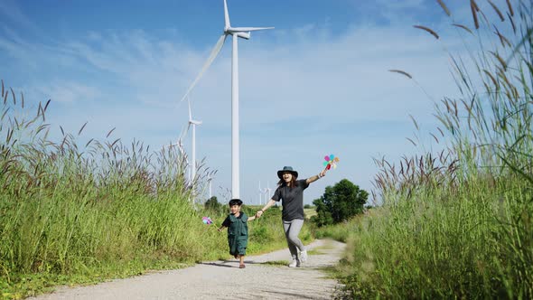 Mother and his son run around with windmills in a wind turbine field,