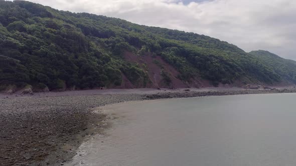 Aerial wide tracking upwards over the sea at the coastline to the west of Porlock Weir, Somerset, En alt