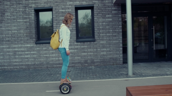 Girl Riding On Hoverboard. Girl Runs Along a Modern Building.
