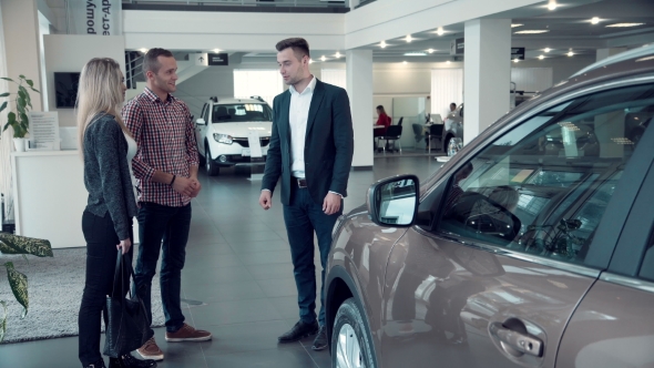 Salesman Talking To Couple Inside Car Dealership alt