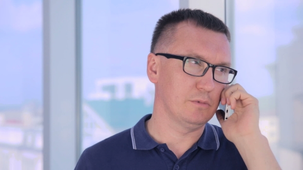 Man Standing At The Office Window Talking With Cellphone. alt