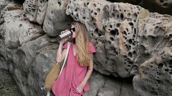 Beautiful Girl in Glasses and with a Thermo Mug Near the Rocks alt