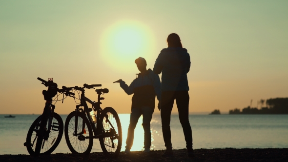 Silhouettes Of Two Cyclists At Sunset. The Pair Finished The Bike Ride