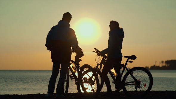 He Silhouettes Of Two People On The Beach With Bikes alt