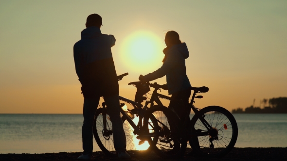Silhouettes Of Cyclists At Sunset. Male And Female Silhouettes