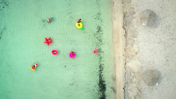Aerial view of friends floating on inflatable mattresses in transparent sea. alt