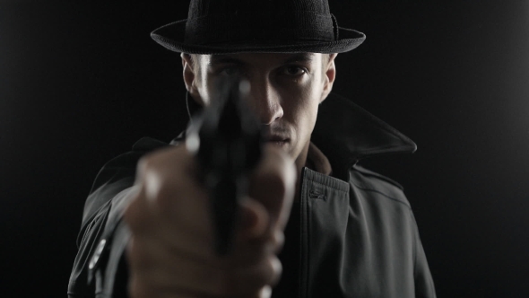Gangster In a Hat And a Black Cloak. Mafioso Aiming a Gun At The Camera alt